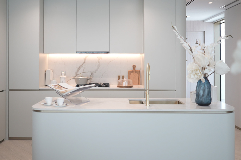 Beach Walk Residence Modern kitchen featuring a minimalistic design, a marble backsplash, island with sink, and decorative flowers.